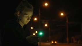 lonely young guy with tied hair with smartphone on the street in the night city, 4k