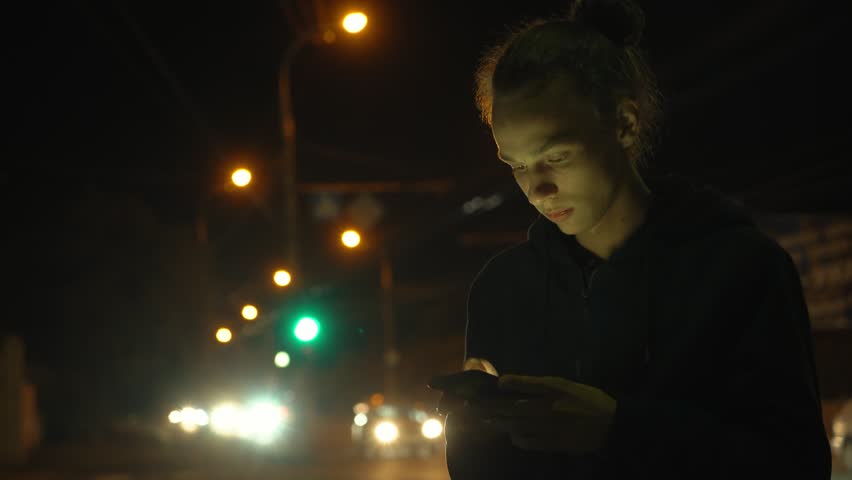 pensive young man waiting for a bus on the street in the city, night traffic, 4k