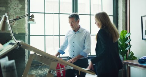 Blonde female architect joins male coworker to go over blueprints in modern high-tech office. Wide to medium shot on 4K RED camera on a gimbal. Stock-video