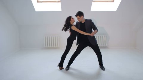 A man and a woman in black clothes dance a sensual dance of salsa or bachata in a white studio. Young couple dancing the salsa or bachata at the dance hall.