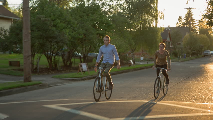 Handheld shot friends cycling on road during sunny day