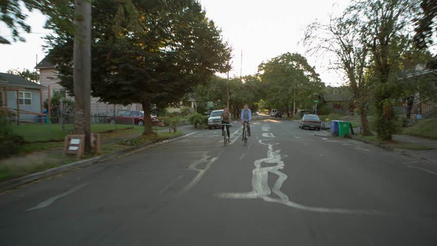 Handheld shot of friends cycling on road amidst houses