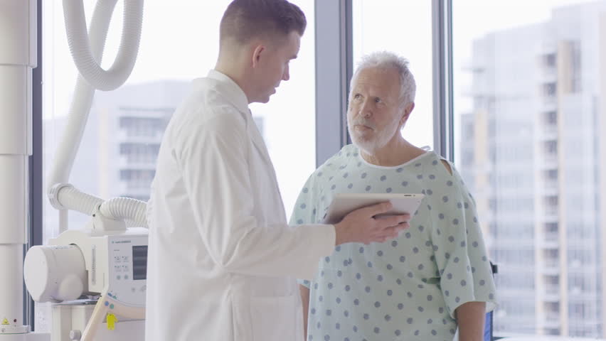 Handheld shot of male doctor explaining to patient over tablet computer in hospital ward | Shutterstock HD Video #1019671684