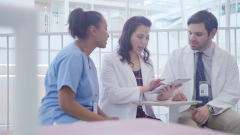 Handheld shot of healthcare workers discussing over tablet computer in hospital corridor