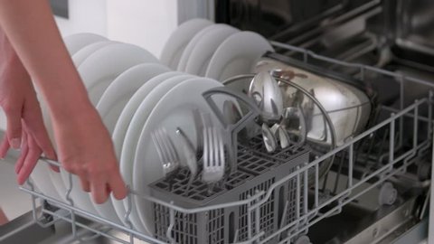 Housewife taking out clean plates from dishwasher machine. Female hands unloading dishwasher close up. Modern appliance at home.