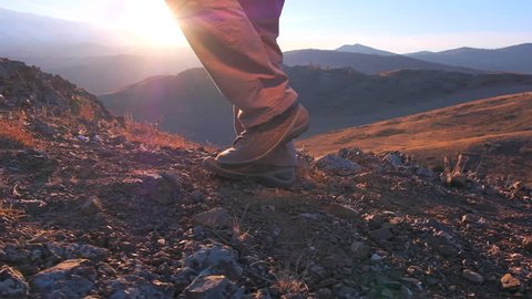 Close up of feet climber male hiker traveler man walking, climbing up in rocky top mountain at sunset. foot steps of hiker man nature travel tourism tourist hiking legs in trekking boots slow motion