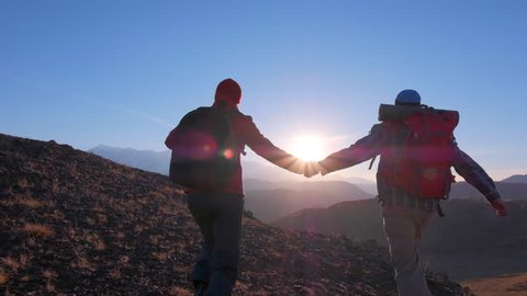 happy tourist couple traveler hiker man woman with backpack climbing up running celebrating success on top mountain at sunset. traveler hikers with raised hands nature travel tourism hiking trekking