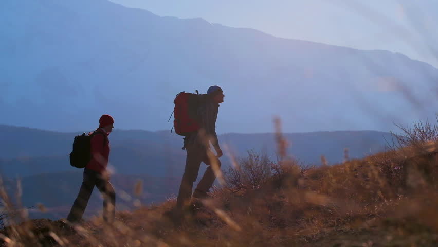 tourist couple traveler hiker man and woman with backpack walking and climbing up on top of mountain at sunset. traveler hikers mountains nature travel active tourism hiking trekking activity summer