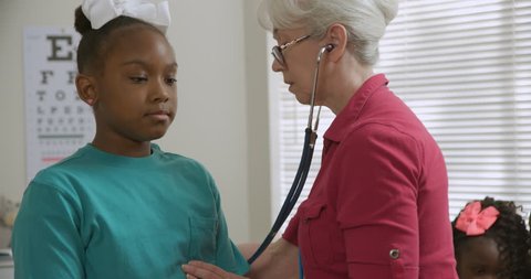 Older Caucasian female pediatrician checks the lung sounds of young African American girl