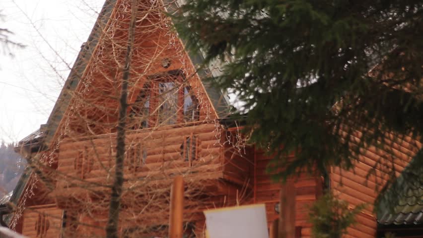 Big wooden house with garland standing in mountains. Weekend out of town. Winter time. Rest. Spruces. Outdoors.