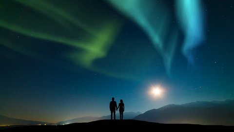 The couple standing on a mountain against a sky with northern light. time lapse