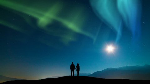 The couple standing on a mountain against a sky with northern light. time lapse