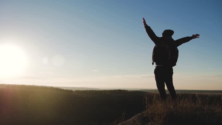Silhouette of person in mountain. Young man with backpack standing with raised hands on top of a mountain. Sport and active life. | Shutterstock HD Video #1019698087