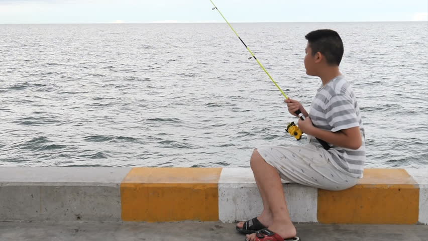 Asian boy fishing at Hua Hin pier in cloudy day.