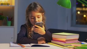 Portrait of little girl using smart phone and making video call talking to her classmates in her room. Communication concept