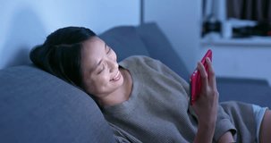 Woman watch on cellphone and lying on sofa at night
