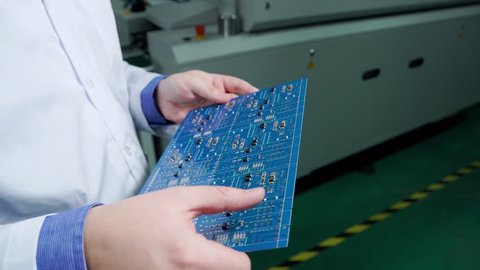 The engineer in a white robe inspect ready motherboard. PCB Processing on CNC machine, Production of electronic components at high-tech factory. Close up