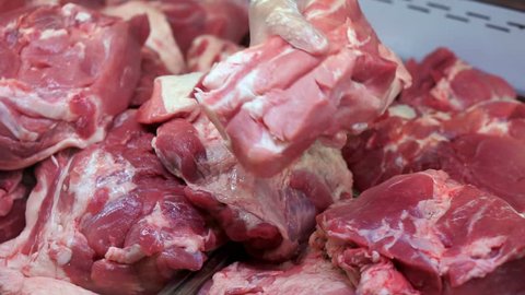 Refrigerator in the store. A pile of raw pork meat. Hand butcher turns over pieces of meat