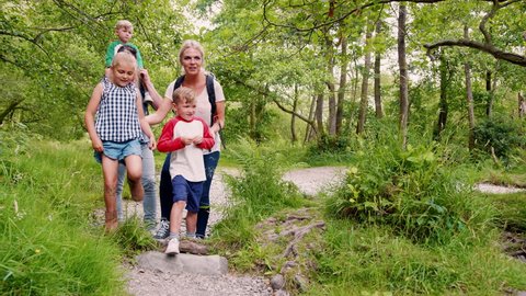Slow Motion Shot Of Family Hiking Along Path By River In UK Lake District