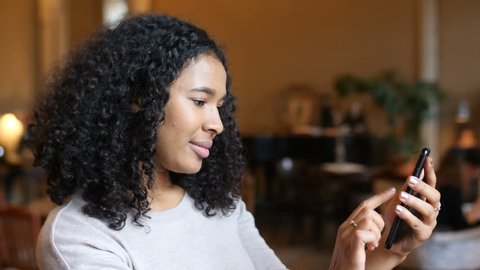 Young African American Black Woman Having Fun Using Smart Phone Technology In Cafe
