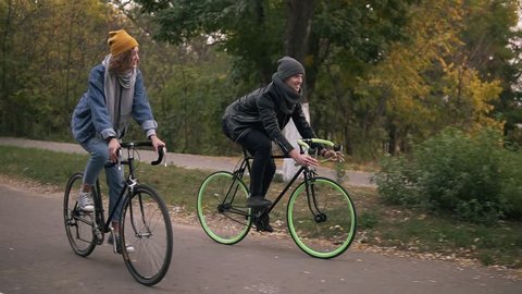 Young hipster couple enjoying cycling through park on trekking bikes. Two young people having great time together in autumn. Side view