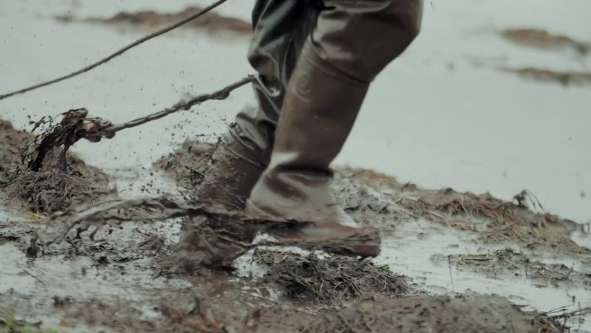 Man walks through the mud in rubber boots