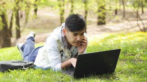 Man lying on meadow with laptop having phone call