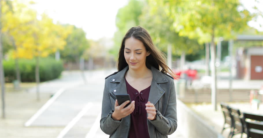 Front view of an excited woman walking towards camera, checking phone and celebrating good news in a park Royalty-Free Stock Footage #1019750314