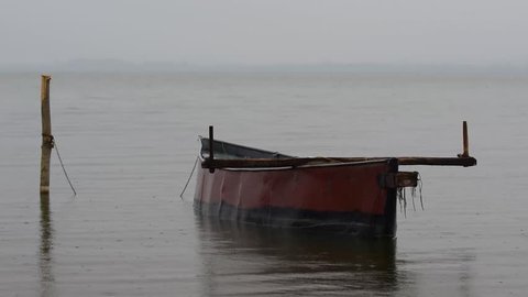 A boat drifting on a lake during rain on a cloudy day.