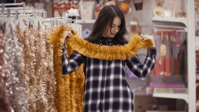 Footage pretty woman buying Christmas decorations. Girl choosing Xmas tinsel. Preparing for the new year
