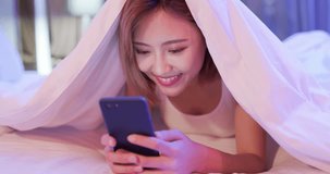 woman use smart phone happily and lying down on the bed under quilt at night