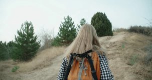 A young girl running on the mountain. In special equipment for a hike and a backpack. Her hair is fluttering in the wind. 4K slow motion video.