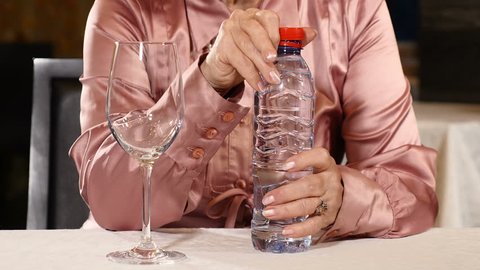 Unrecognizable retired woman sits in restaurant opening a bottle of still water.