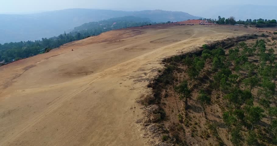 Drone footage of Table Land, Panchgani in the surroundings of Mahabaleshwar, Maharashtra, India, with a flat rocky plateau on top of a hill, a few trees are scattered along its edge. The camera is fol