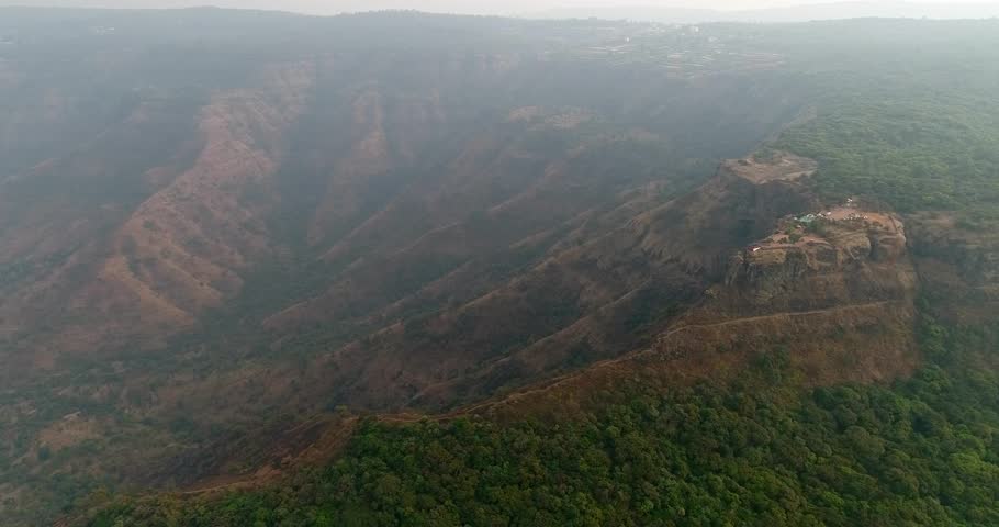Drone footage of Elephant Head Rock in the surroundings of Mahabaleshwar, Maharashtra, India, with a touristic view point on a cliff and the steep rocky hill side covered in low tropical vegetation. T