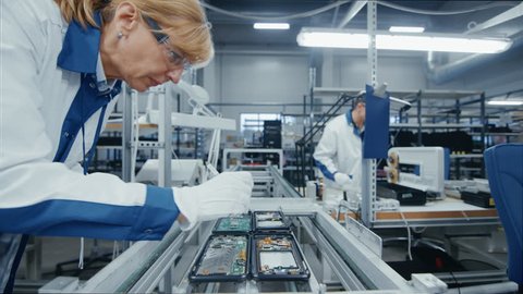 Time Lapse of Electronics Factory Workers Assembling Smartphone Circuit Boards by Hand While they Move on the Assembly Line. High Tech Factory Facility. 