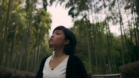 Young beautiful woman walking through a pathway in a bamboo forest in Kyoto, Japan with soft natural lighting. Medium wide shot on 4k RED camera.