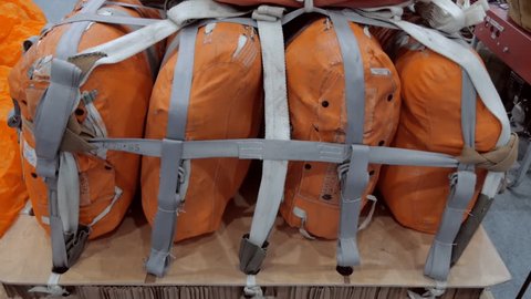 On the wooden pallet there are several orange bags with things and equipment fastened with a strap and with a laid parachute on top, ready to be dropped from an airplane. Shot in motion