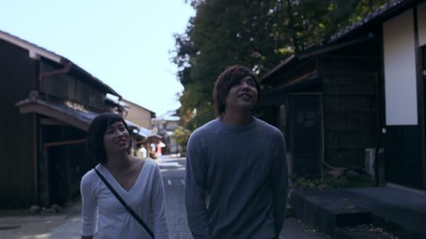 Two friends laughing and talking while walking down a sidewalk in Kyoto, Japan with soft shaded lighting. 