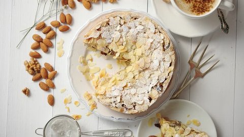 Shot of a whole round delicious apple cake tart with almond flakes served on wooden table. With coffee in a cup and slice of a pie on soucer.