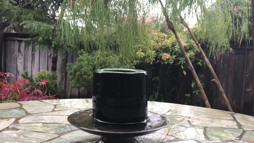 Rain falls on a teacup that sits on a saucer on a stone table in the garden.  Includes rain sounds.