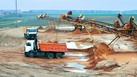 Mining site with heavy industrial equipment. Mining elevator with belt conveyor loading sand in dumper truck. Heavy machinery in mining industry