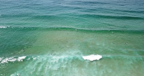 Aerial view of surfers catching waves in crystal clear water of Australian pacific coast