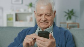 Portrait of Progressive Senior Man Sitting in His Living Room Easily Uses Smartphone, Does Touching and Swiping Gestures and Feels Very Comfortable with New Technologies.