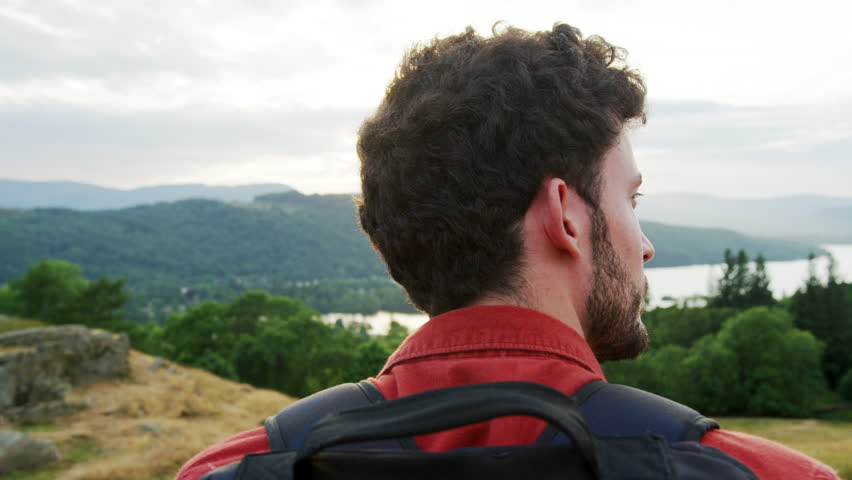 A young adult Caucasian man standing at the summit admiring the view during a mountain hike, close up, back view