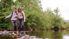 A young adult couple hold hands while crossing a stream balancing on stones during a hike - Powered by Shutterstock - Get 15% off with code: PIKWIZARD15