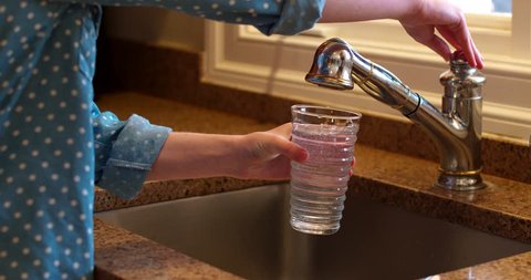 Young Woman fills Water Glass with Tap Water at Nice Sink with Granite Counter Top