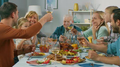 Big Family and Friends Celebration at Home, Diverse Group of Children, Young Adults and Old People Gathered at the Table have Fun Conversation. Clinking Glasses and Making Toast. In Slow Motion.