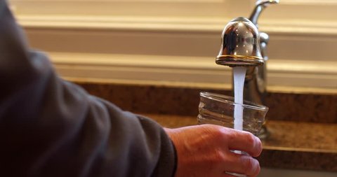 Man fills Water Glass with Tap Water at Nice Sink with Granite Counter Top