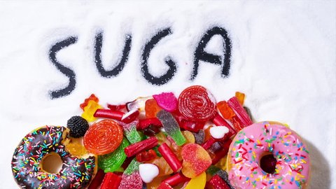Doughnuts and candies on refined sugar where the text Sugar is Bad is written in stop frame animation. Health and sugar addiction concept.